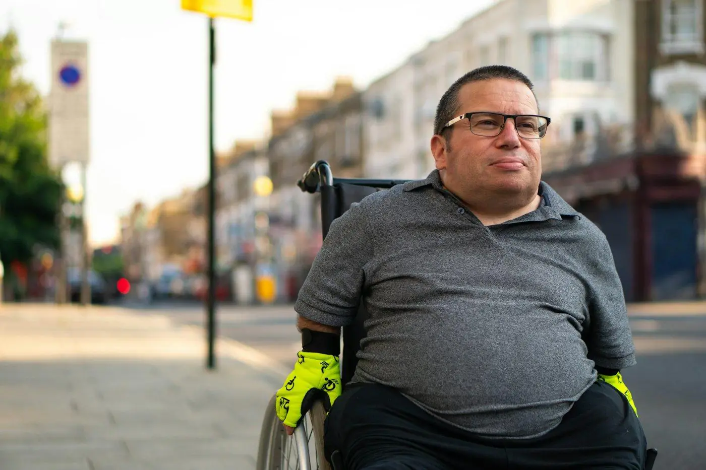 A smiling man using a wheelchair on a sunny city street