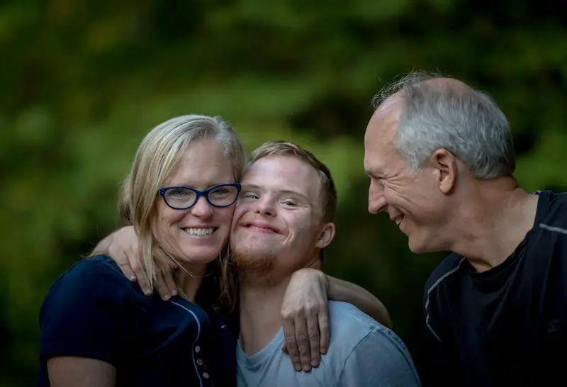 A young man with Down syndrome hugging his smiling parents
