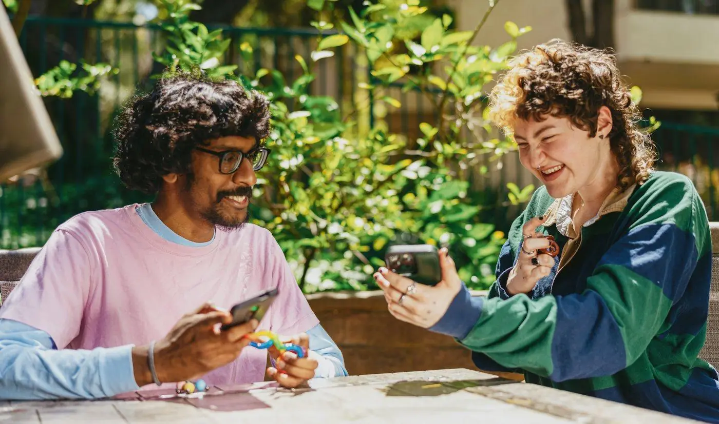 Two friends sitting outdoors, laughing as they look at their phones