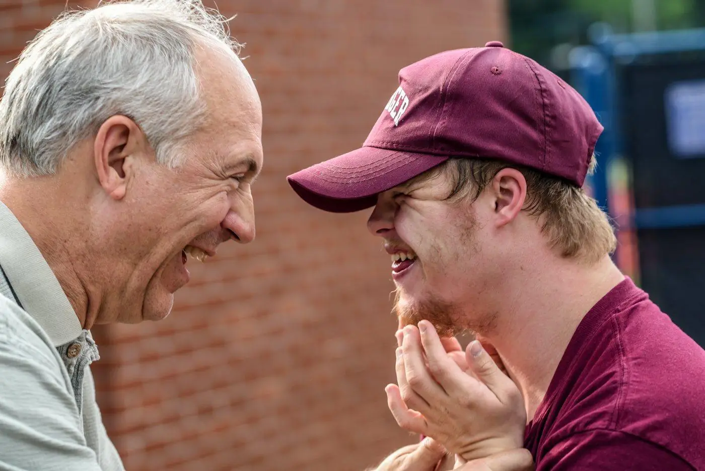 A young man and an older man sharing a big laugh outdoors